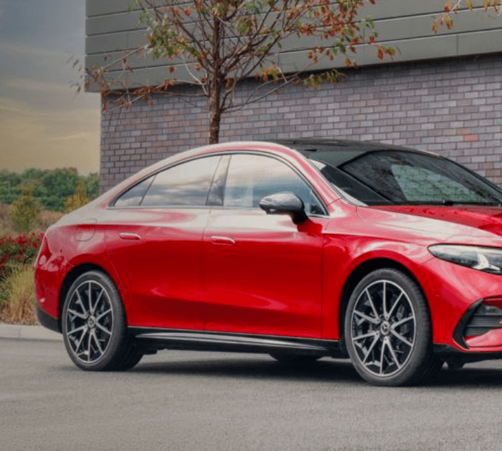 Sleek red Mercedes-Benz sedan parked in front of a modern brick building at sunset.